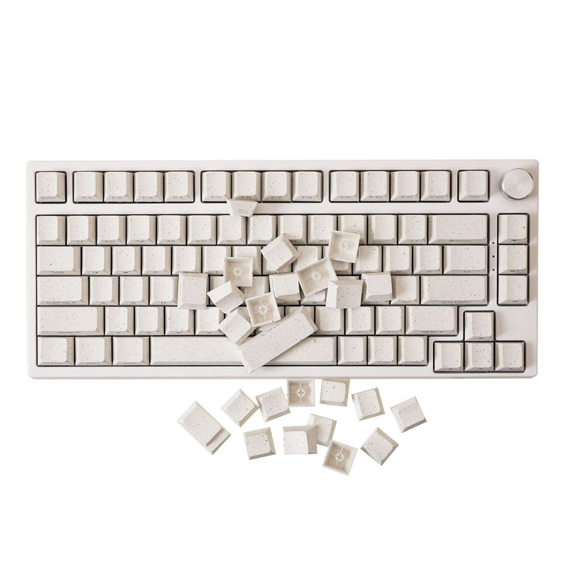 Gamakay 122 Keys Shine Through Custom Keycaps Set displayed on a keyboard with several keycaps scattered on and around the keyboard. The keycaps feature a speckled design and are crafted to enhance backlighting effects.